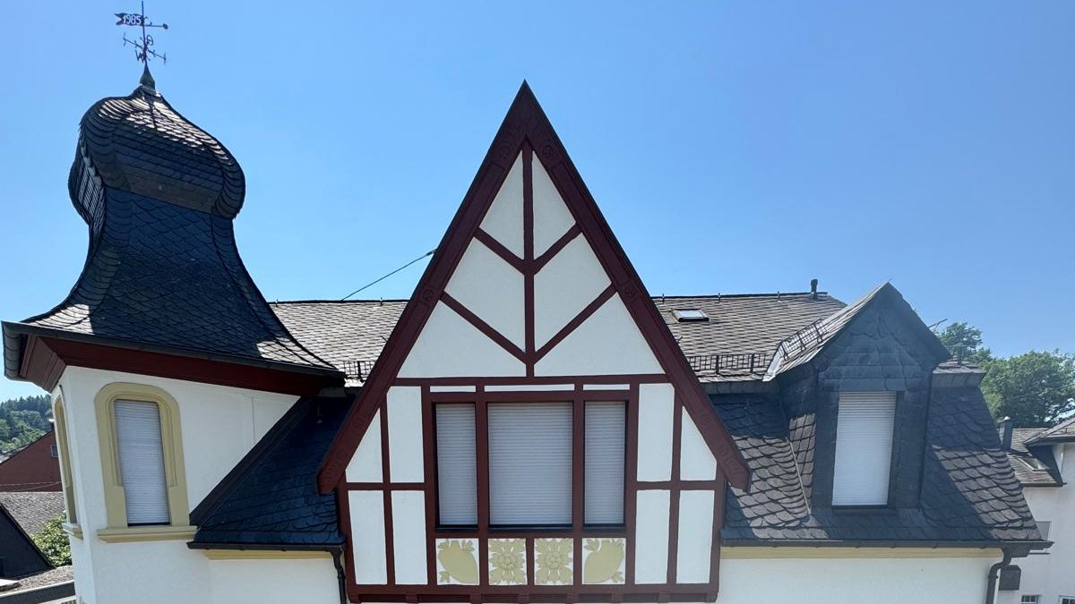Frisch renovierte Jugendstilvilla mit Ecktürmchen, Zierfachwerk und hellem Anstrich vor blauem Himmel.
