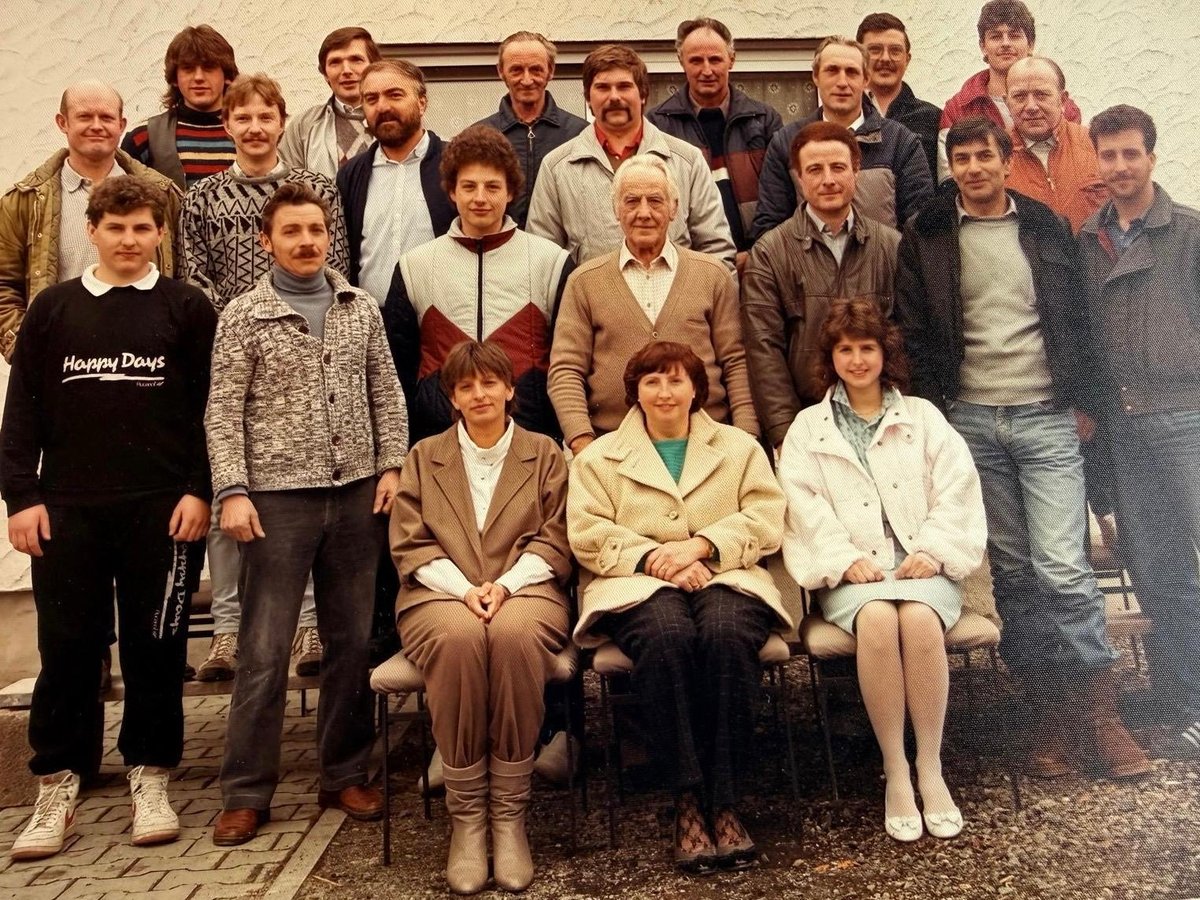 Gruppenfoto der Belegschaft: rund zwanzig Personen in mehreren Reihen vor einer hellen Hauswand.