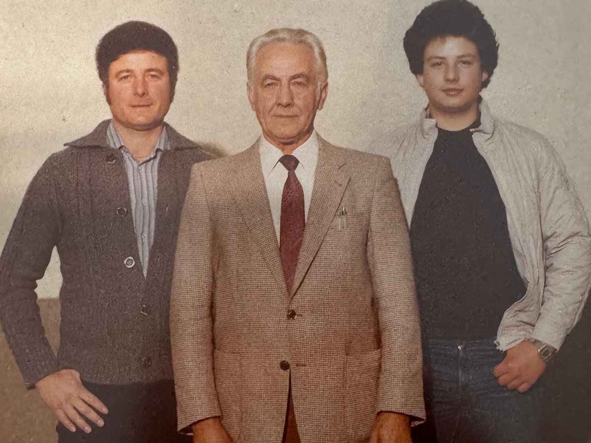 Drei Männer verschiedener Generationen stehen nebeneinander vor einer hellen Wand.