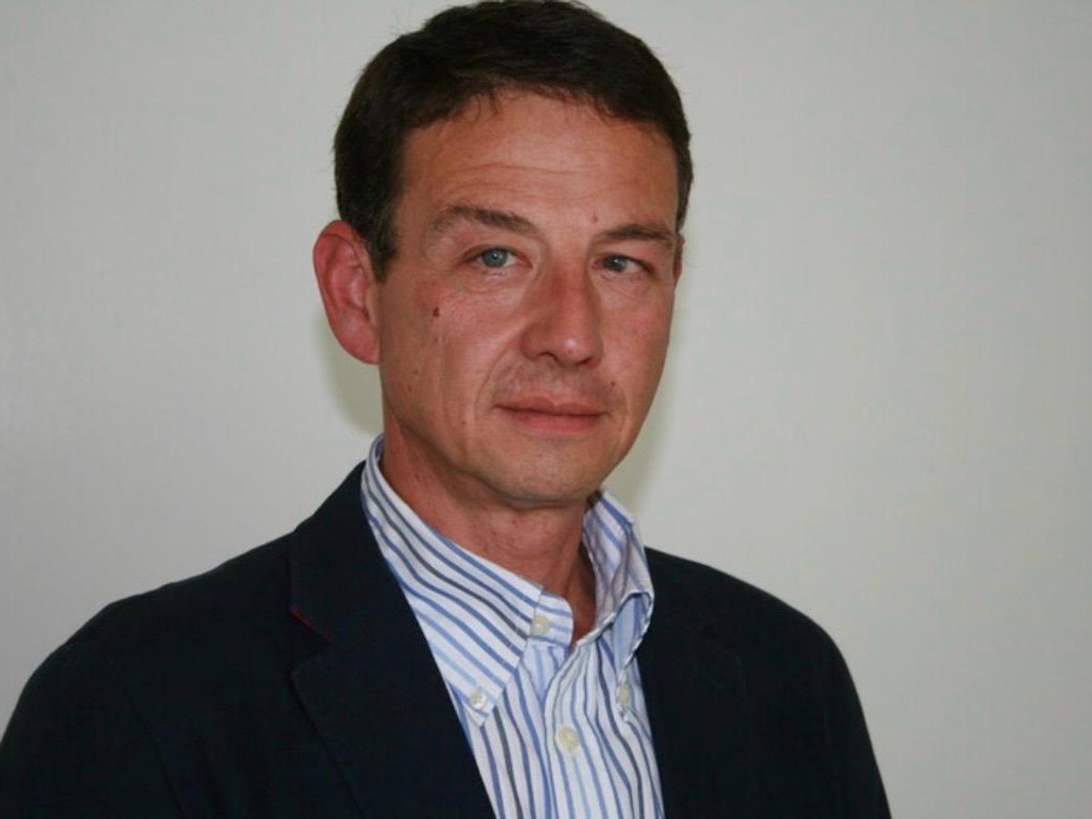 Porträtaufnahme von Ralf Magard vor heller Wand, dunkles Sakko über hellem Streifenhemd.
