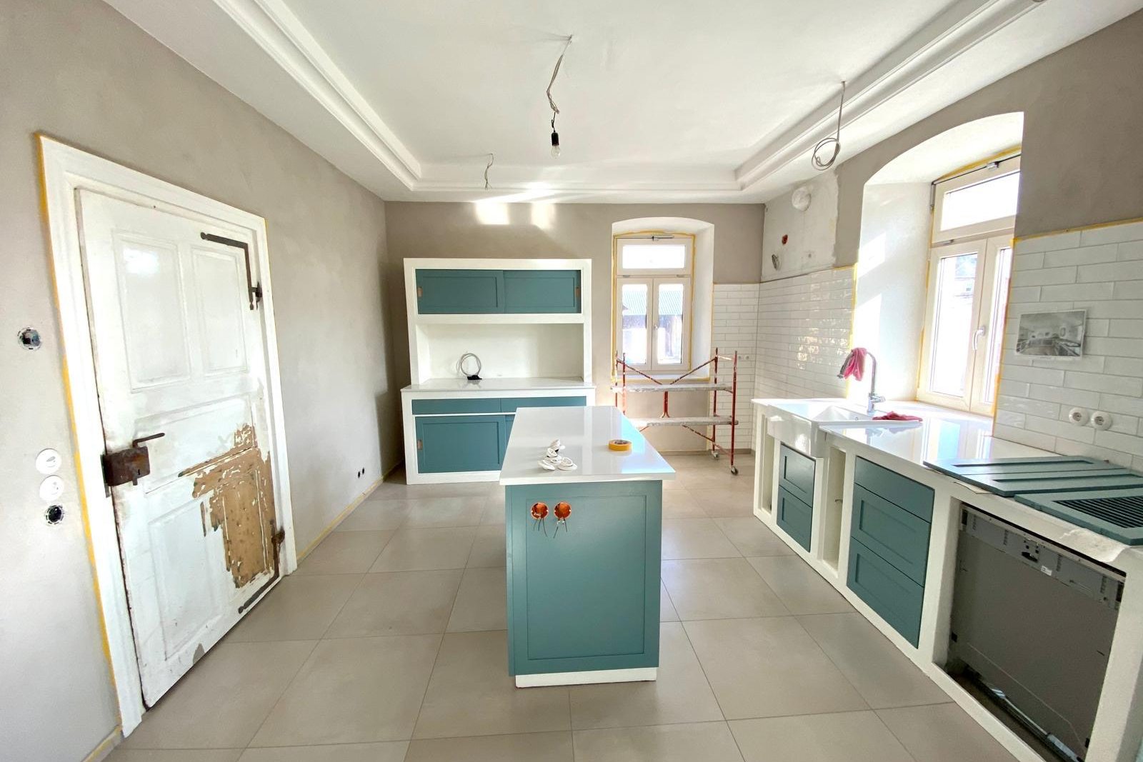 Renovierte Küche im Altbau mit Stuckdecke, Kochinsel und petrolfarbenen Möbelfronten.