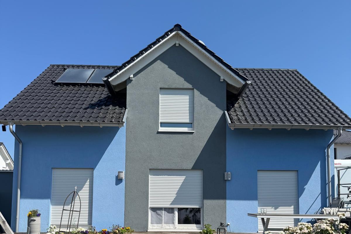 Einfamilienhaus von der Gartenseite: die verputzte Fassade ist hellblau gestrichen, der vorspringende Giebel graublau abgesetzt.