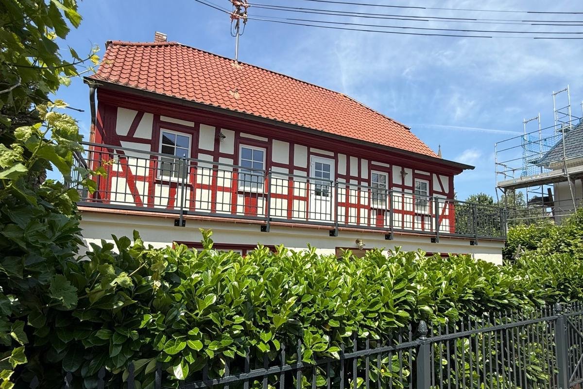 Fachwerkhaus mit frisch gestrichenem rot-weißem Fachwerk hinter einem schwarzen Metallzaun.