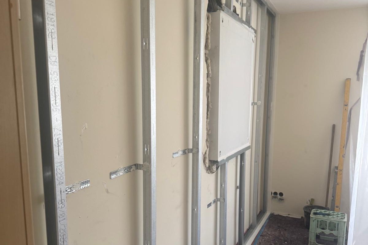 Vorsatzschale im Bau: senkrechte Metallprofile stehen vor einer hellen Wand, an Winkeln befestigt und um einen Wandkasten herum ausgespart.