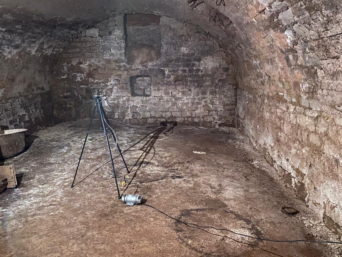 Gewölbekeller aus Bruchstein im Rohzustand, auf dem Boden ein Messgerät auf einem Stativ und ein Gerät mit Kabel.