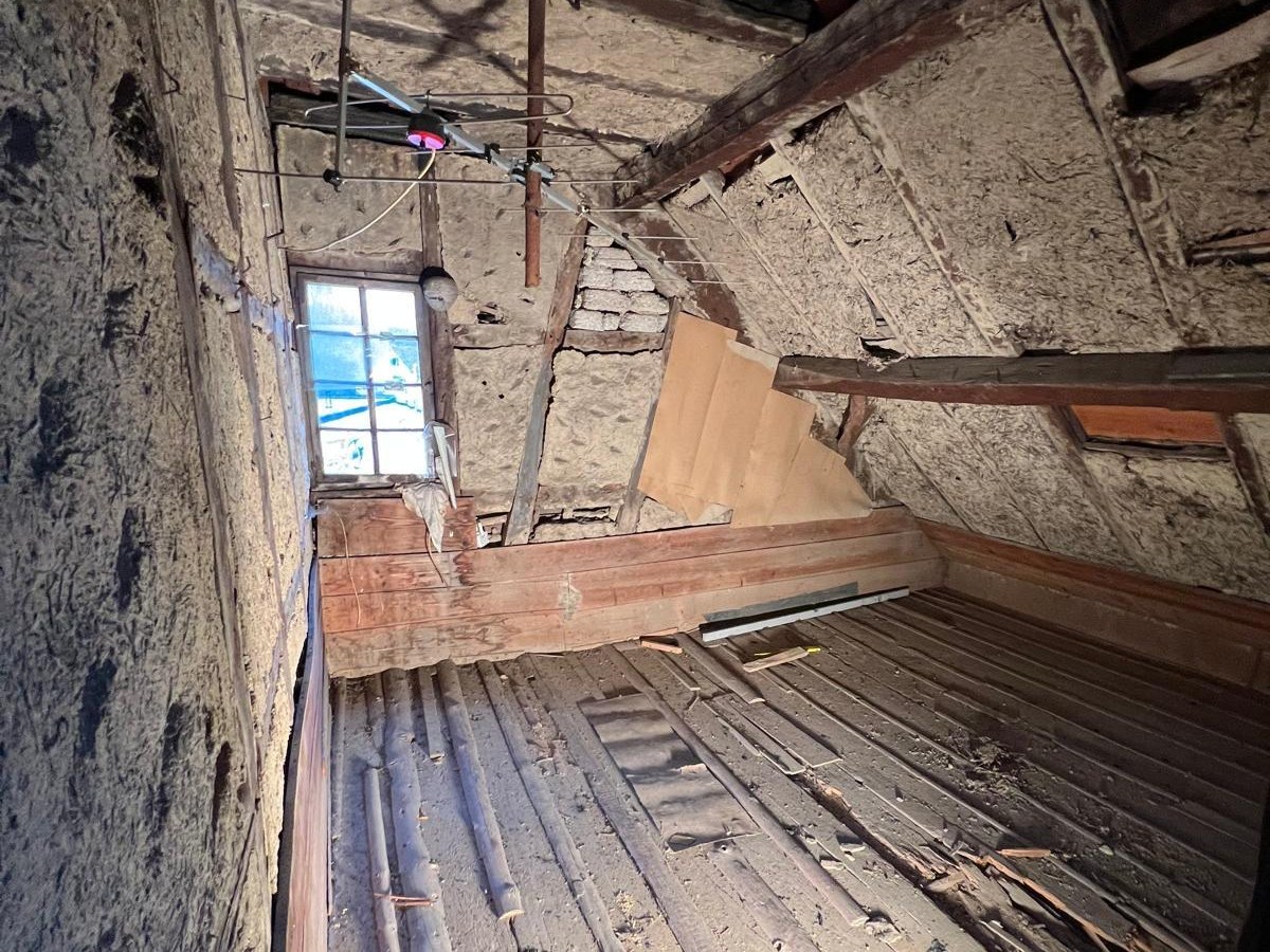 Dachboden im Rohzustand mit alter Balkenlage, aufgerissenen Dielen und historischer Deckenkonstruktion.