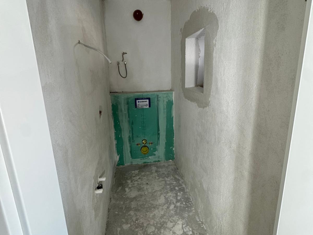 Schmales Gäste-WC im Rohbau mit verputzten Wänden, Vorwandelement und vorbereiteten Anschlüssen.