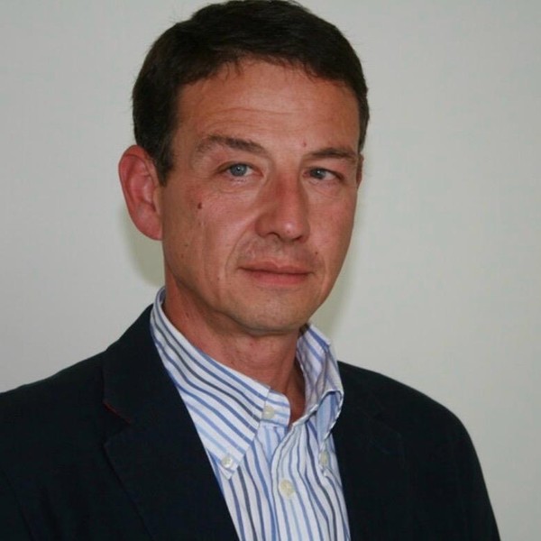 Ralf Magard, Porträtaufnahme vor heller Wand, dunkles Sakko über hellem Streifenhemd.